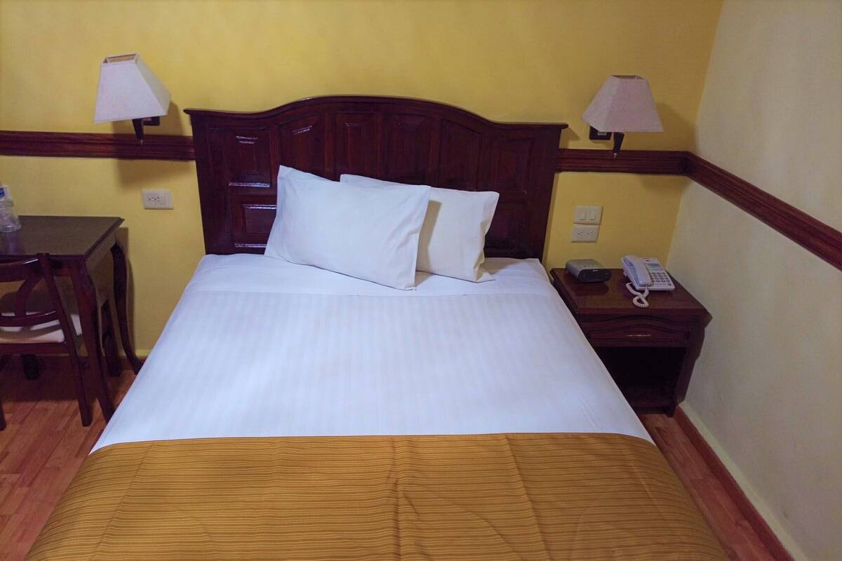 A neatly made bed with a wooden headboard, two bedside tables with lamps, and a telephone on the right side.