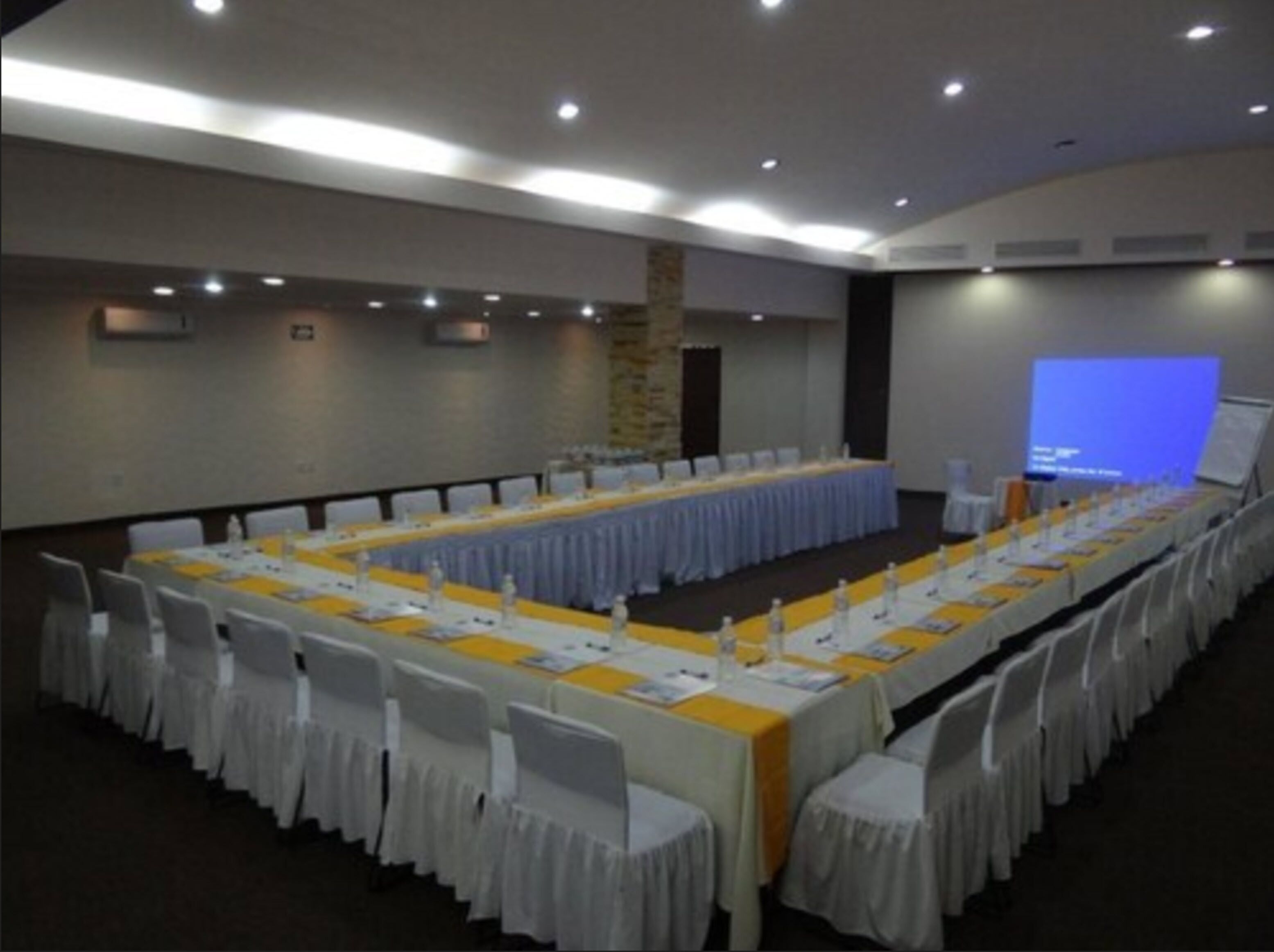 A conference room with long tables, white chairs, and a projection screen.