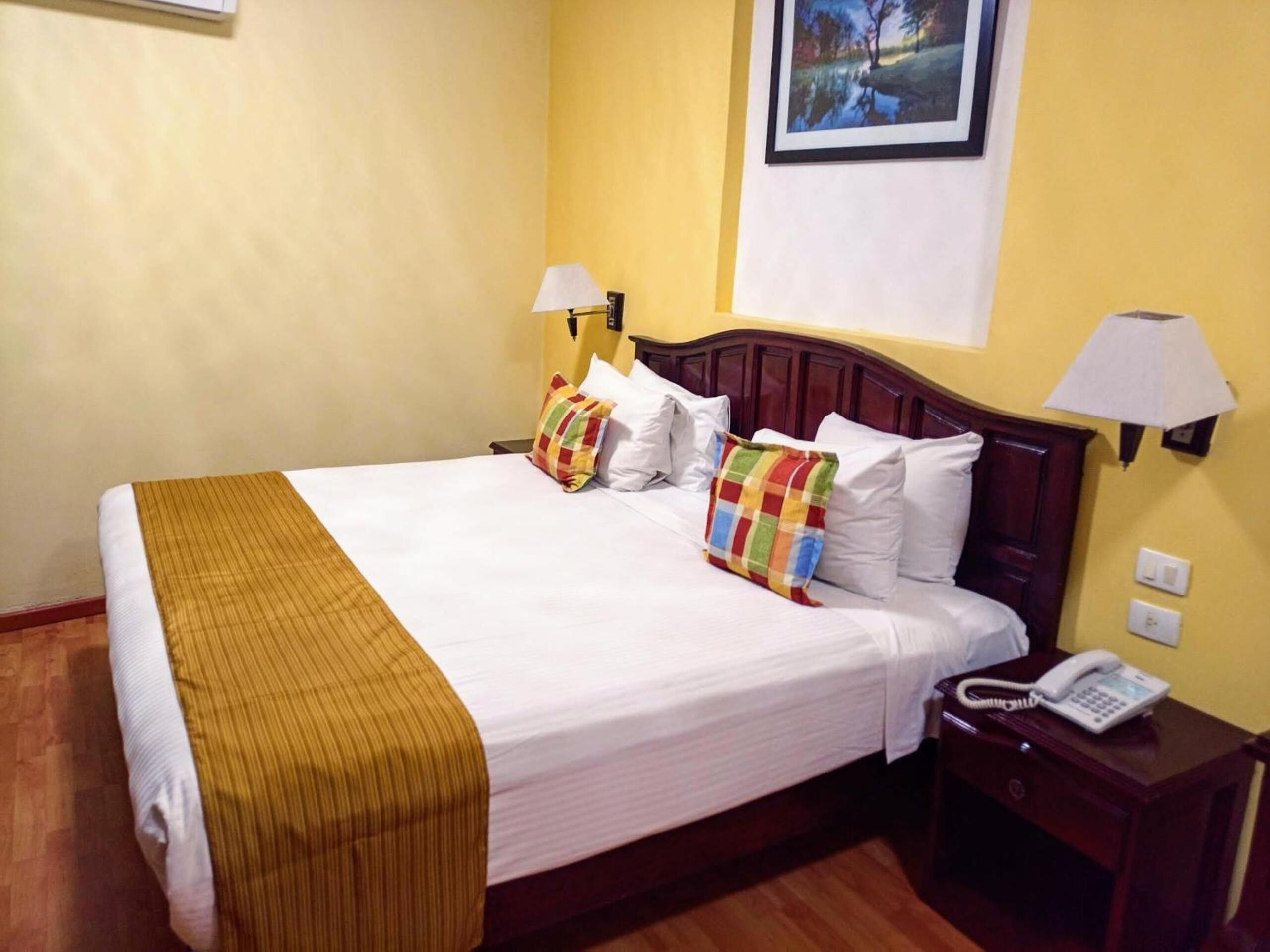 A hotel room with a large bed, two bedside lamps, a telephone, and a framed picture on the wall.