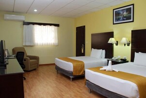 Habitación de hotel con dos camas, un escritorio con computadora, una silla y una ventana con cortinas.