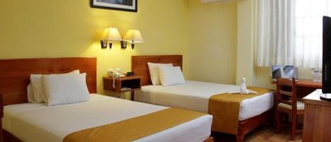 A hotel room with two beds, a desk, a chair, a TV, and an air conditioning unit.