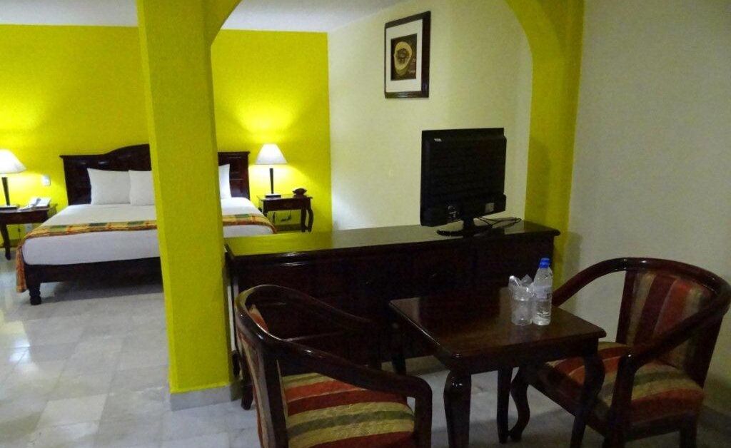 A hotel room with two beds, a desk with a TV, and two chairs.