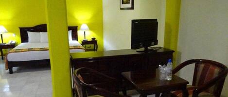 A hotel room with two beds, a desk with a TV, and two chairs.