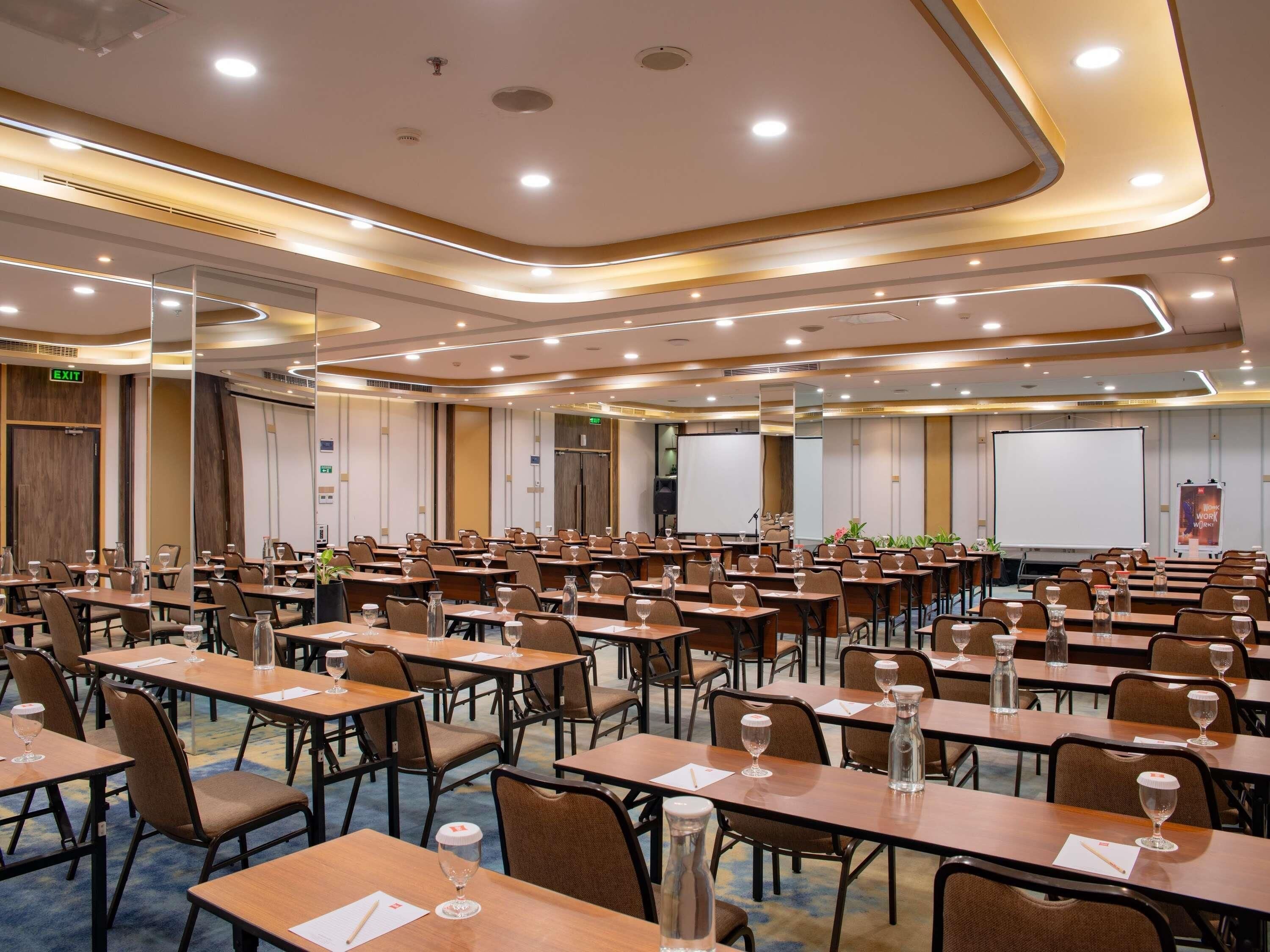 Un salón de conferencias con varias mesas, sillas y una pantalla para proyector.