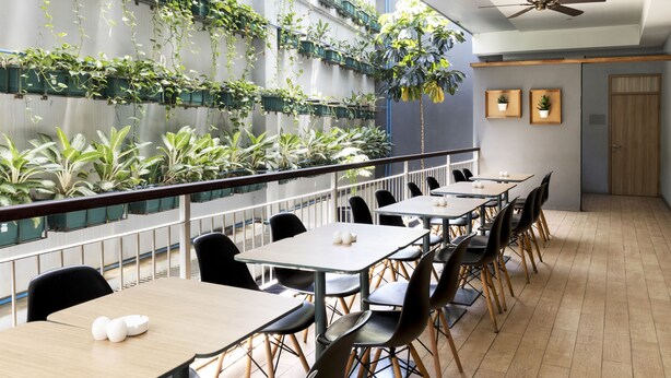 A modern dining area with tables and chairs, a balcony with plants, and a ceiling fan. - Ibis Bandung Pasteur (Bandung)