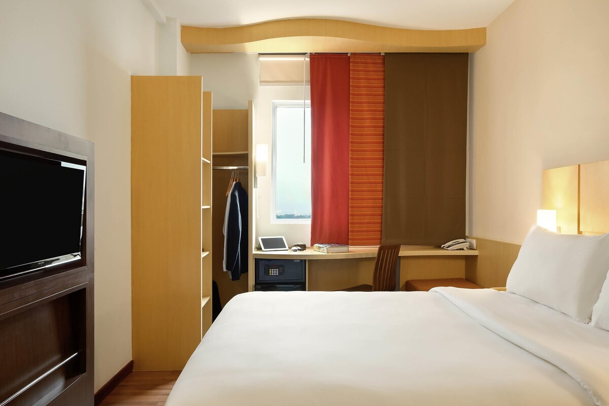 A hotel room with a bed, a desk with a computer, a telephone, and a television.