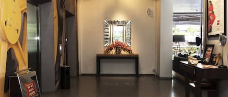 A reception area with a bench, a mirror, a flower arrangement, and a signboard.