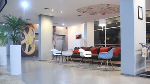 A modern lobby with a large clock mural, a reception desk, and a seating area with a red sofa and white chairs. - Ibis Bandung Pasteur (Bandung)