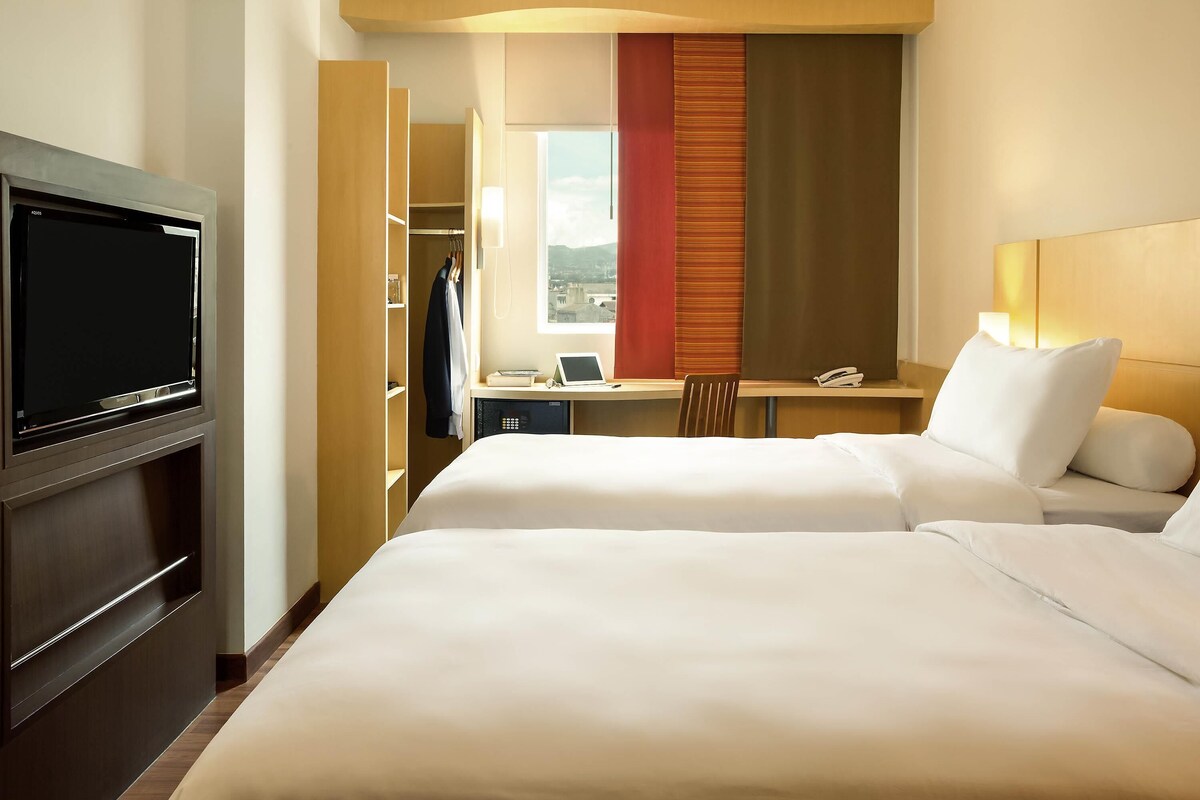 A hotel room with a bed, a desk with a computer, a TV, and a wardrobe.
