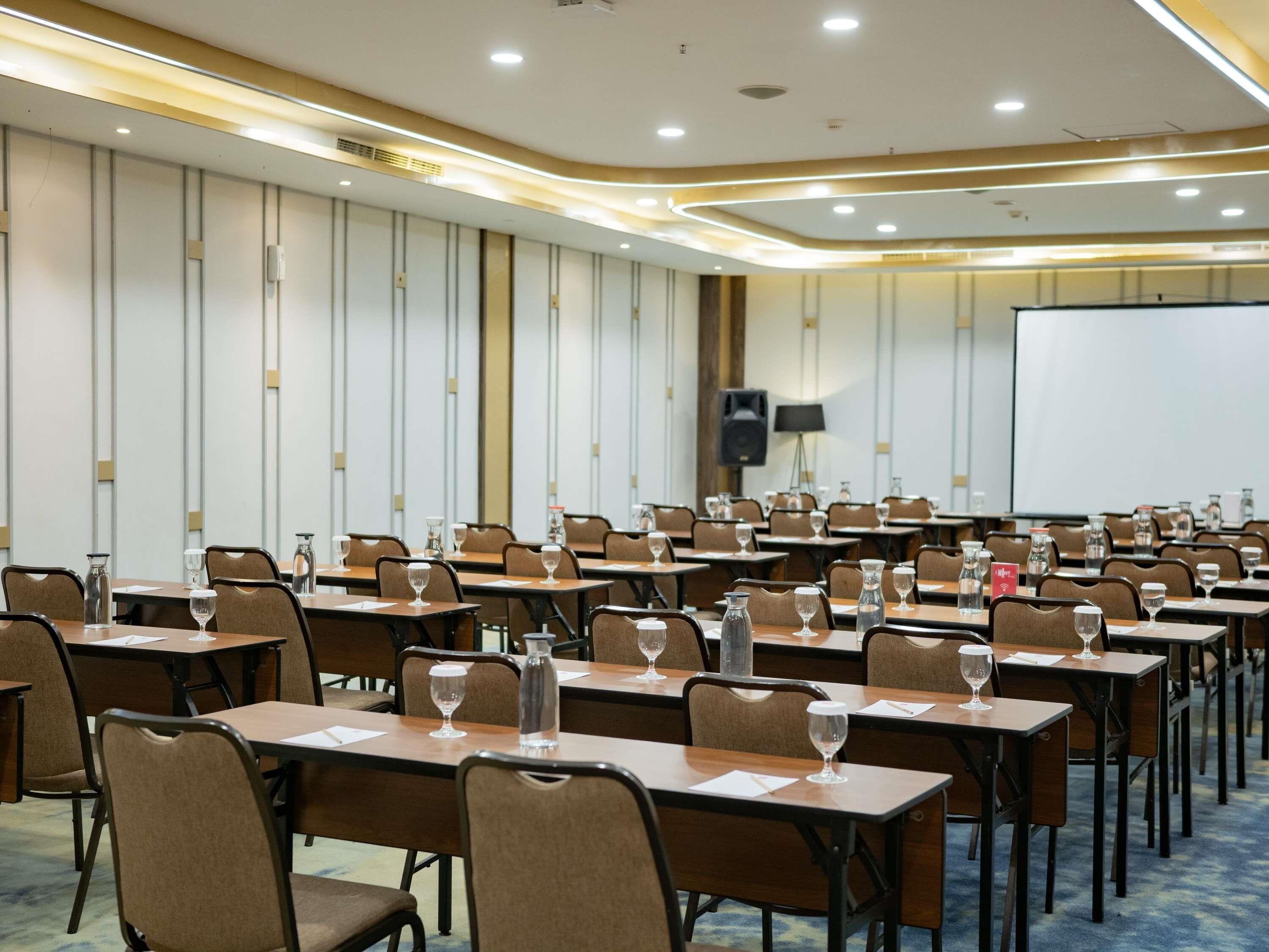 A conference room with tables, chairs, a projector screen, and a speaker.