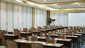 A conference room with tables, chairs, a projector screen, and a speaker.