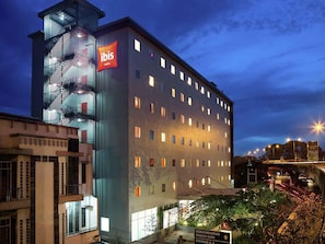 Un hotel moderno con un cartel llamativo de 'ibis Hotels', varios pisos y una escalera a la izquierda.