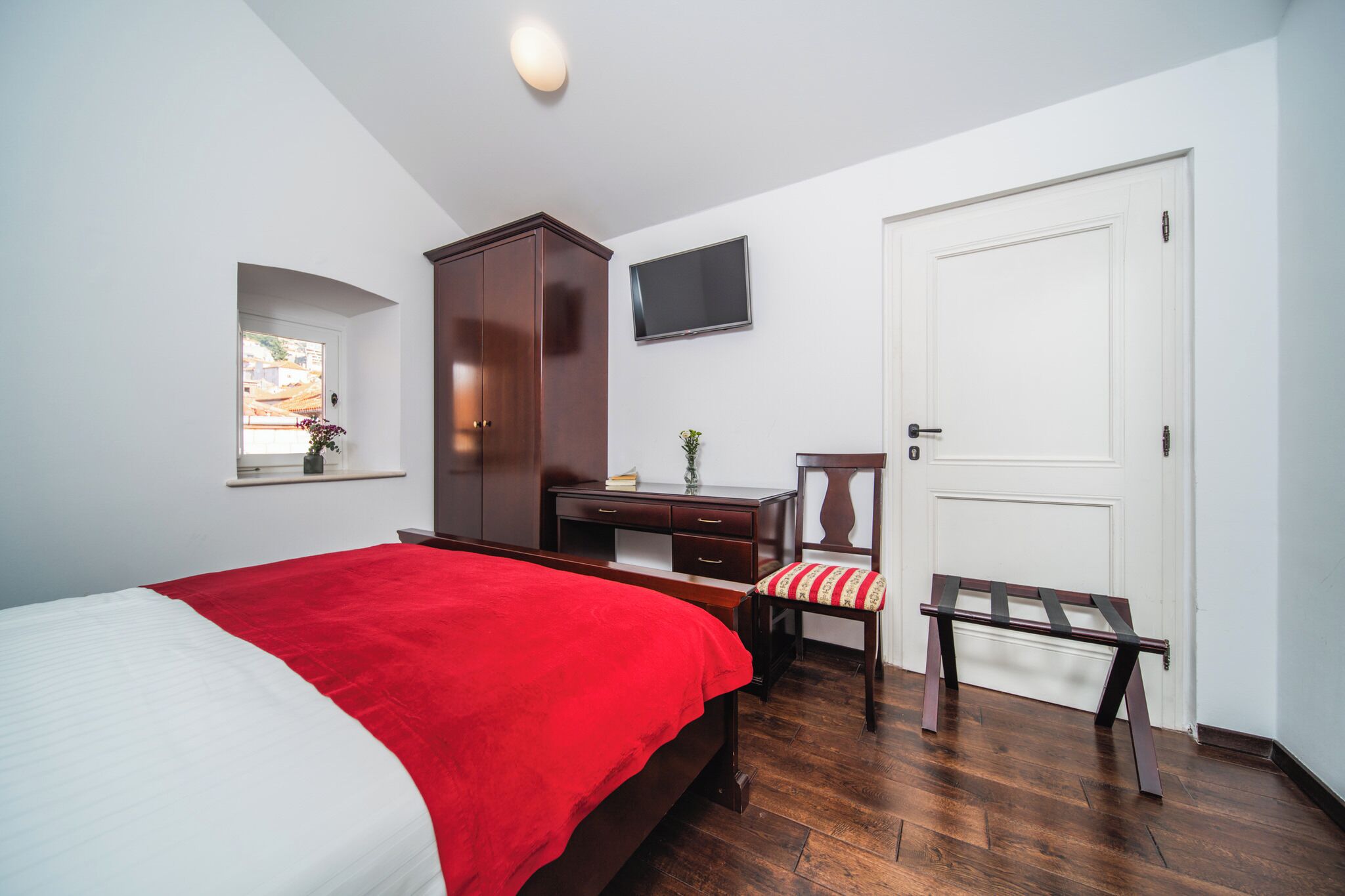 Un dormitorio con cama, escritorio, silla, televisor y puerta.