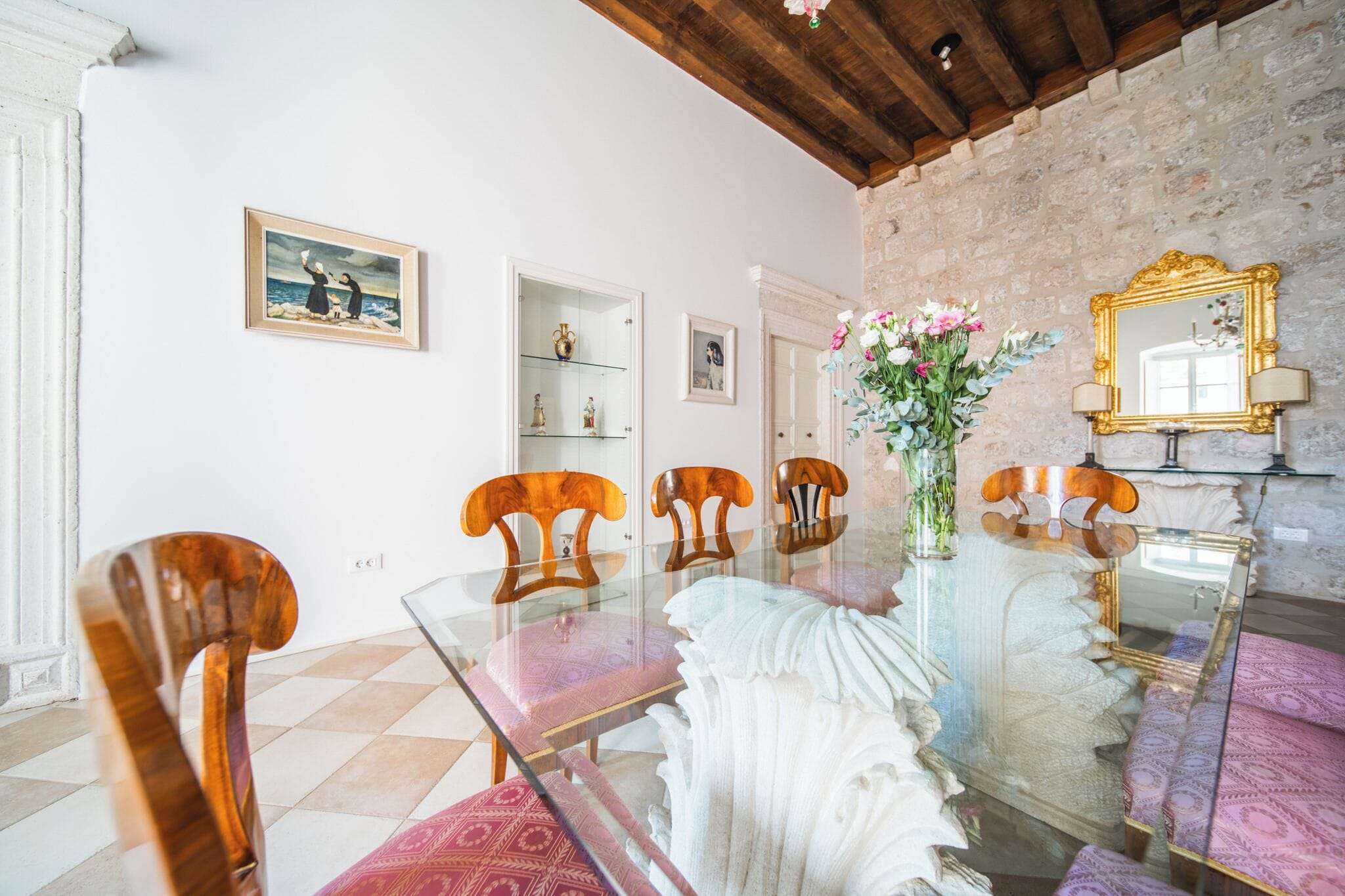 A dining area with a glass table, wooden chairs, and a vase of flowers.