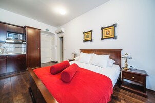 Quarto de hotel com cama, mesa de cabeceira, luminária, micro-ondas e cozinha.