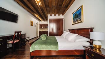 A bedroom with a wooden bed, a green throw blanket, a bedside lamp, and a painting on the wall.