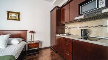 Une chambre d’hôtel compacte comprenant un lit, une table de chevet, une lampe, une kitchenette équipée d’un four à micro-ondes et d’un évier, ainsi qu’un tableau encadré au mur.