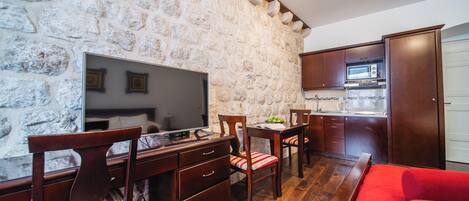Habitación con pared de piedra, muebles de madera, televisor de pantalla plana, sofá rojo y una zona de cocina.