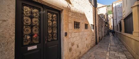 Une ruelle étroite pavée, bordée de bâtiments historiques aux murs de pierre et aux portes noires traditionnelles.