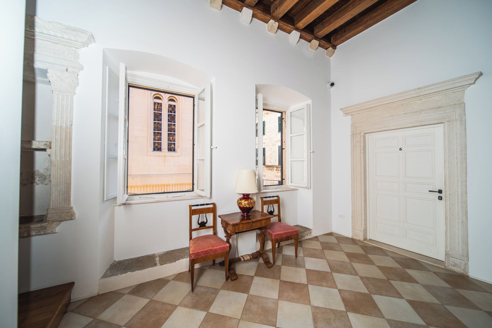 A room with a checkered floor, a table with chairs, and a door marked with the number 6.