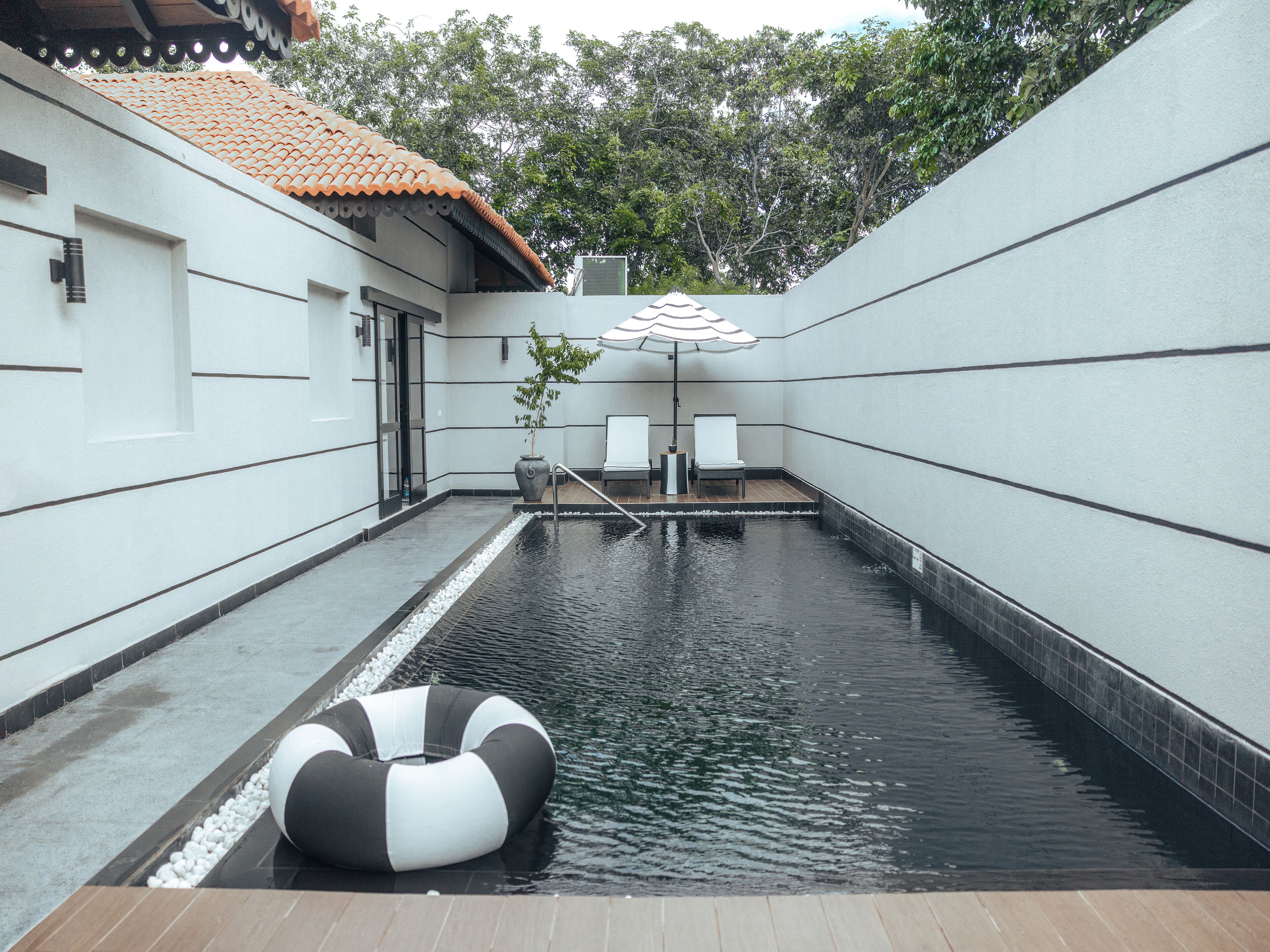 A swimming pool with a lifebuoy, two chairs, and an umbrella.