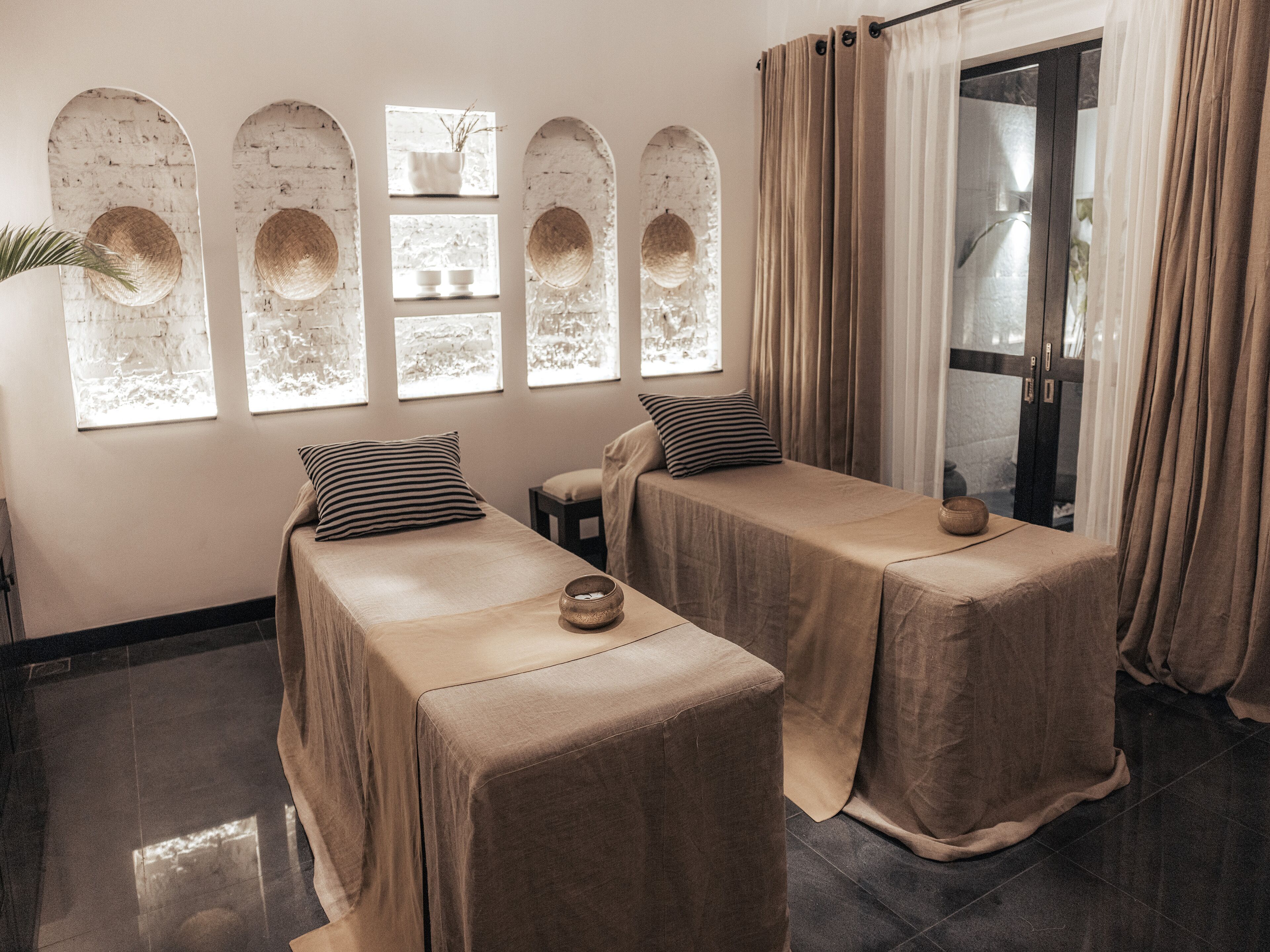 A room with two beds, a window with decorative arches, and a view of the outside.