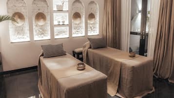 A room with two beds, a window with decorative arches, and a view of the outside.