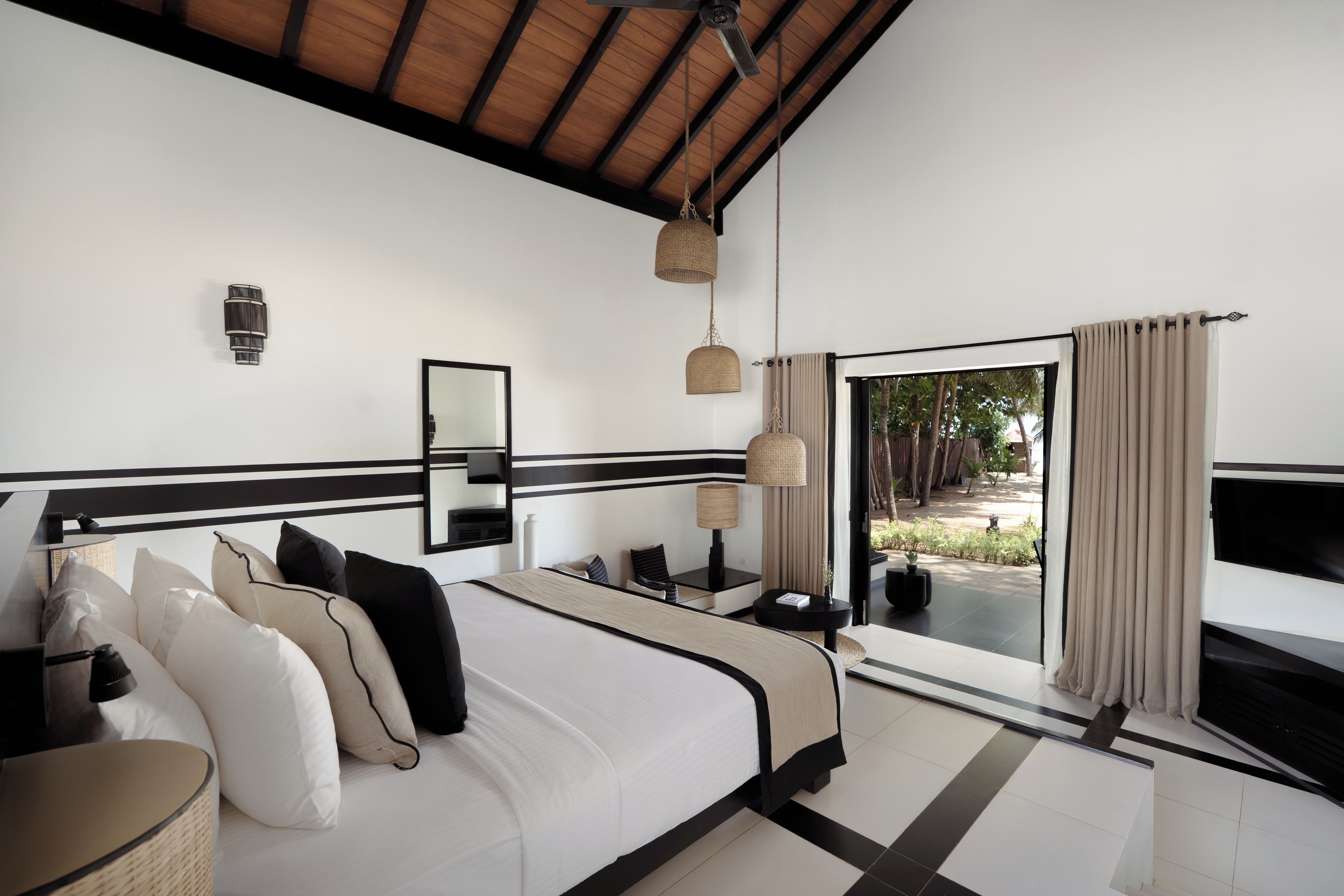 A modern bedroom with a large bed, bedside tables, a mirror, and a view of the outdoors.