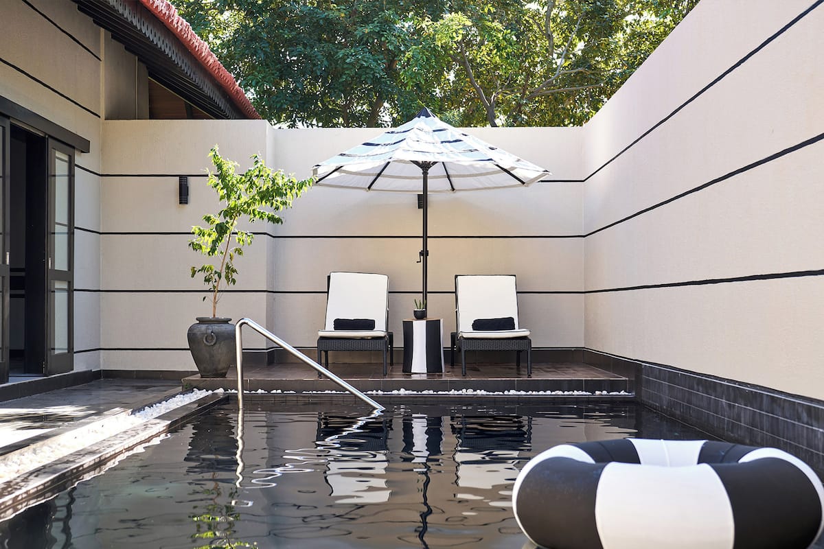 A serene indoor pool area with two lounge chairs, a potted plant, and a floating water toy.