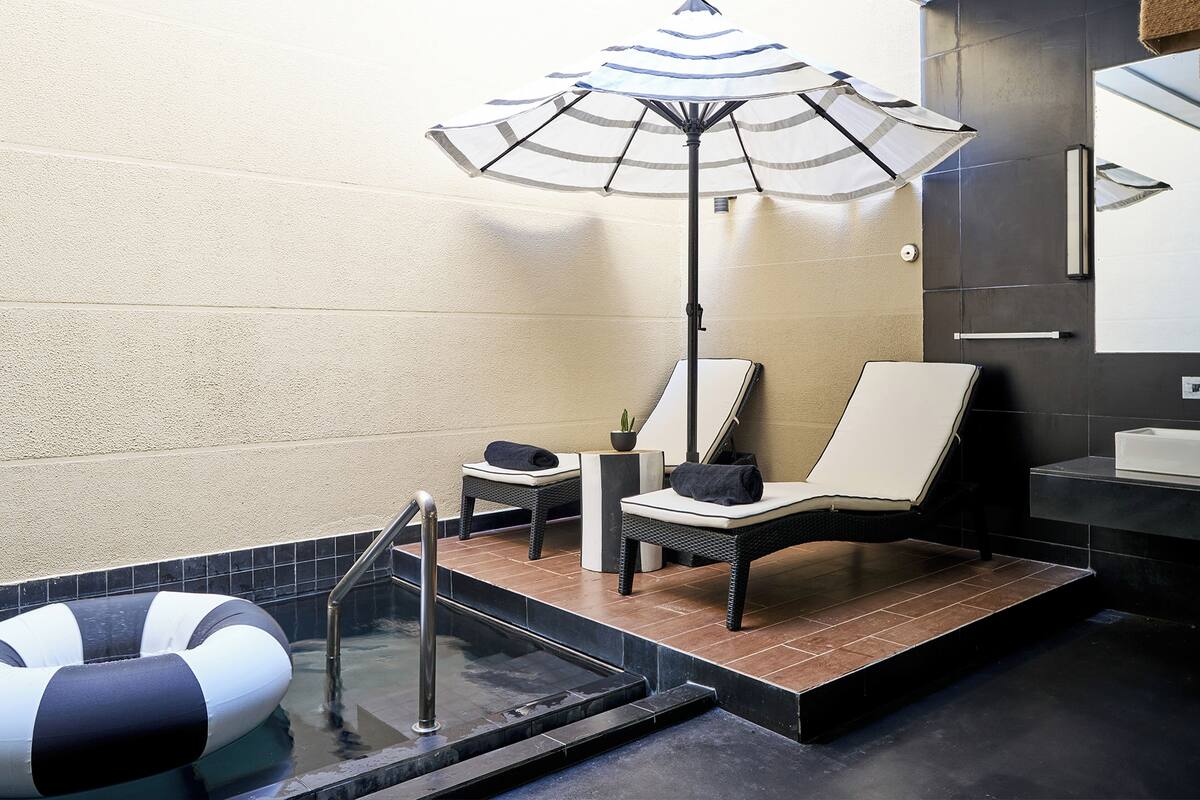 A modern bathroom with a bathtub, a lounge chair, a small table with a plant, and a large umbrella.
