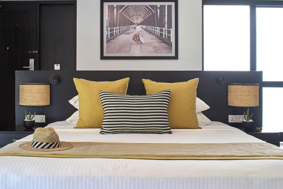 A hotel room with a large bed, two bedside lamps, a framed picture on the wall, and a hat on the bed.