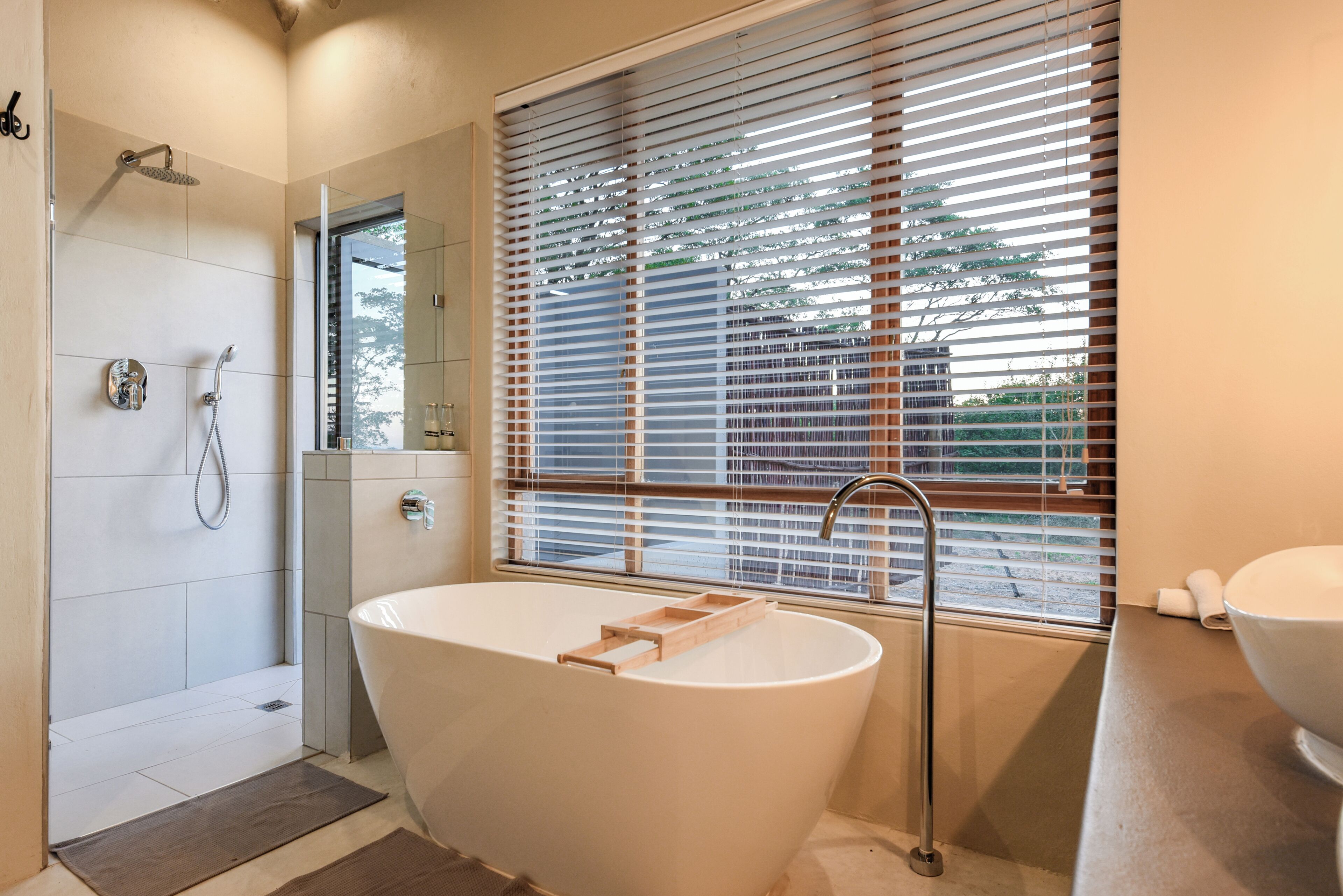 Un baño moderno con una bañera independiente, ducha y ventana con persianas.