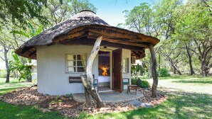A small, thatched-roof hut with a wooden door, surrounded by a stone pathway and lush greenery.