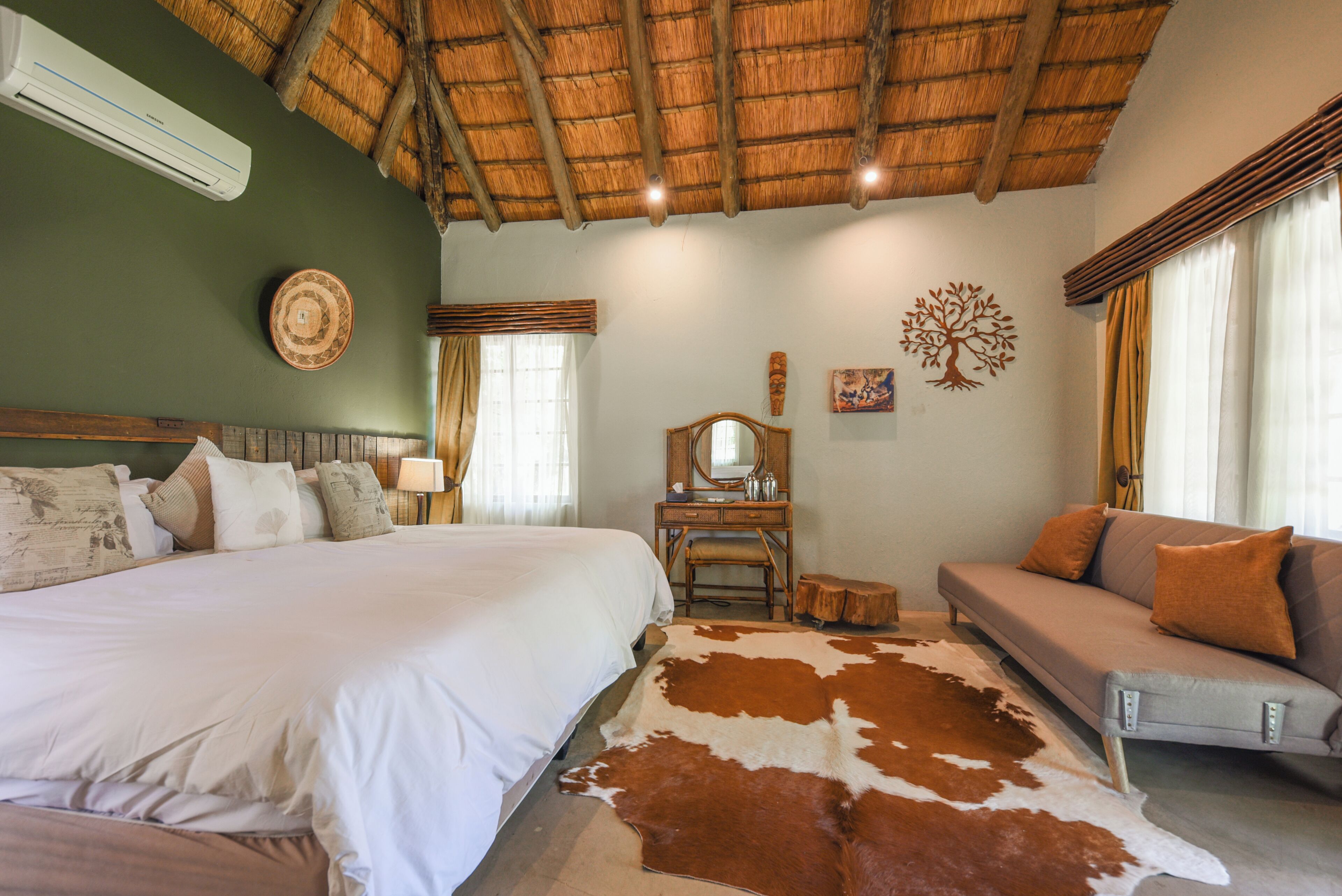 A room with a bed, a sofa, a wooden dresser, a mirror, and a cowhide rug.