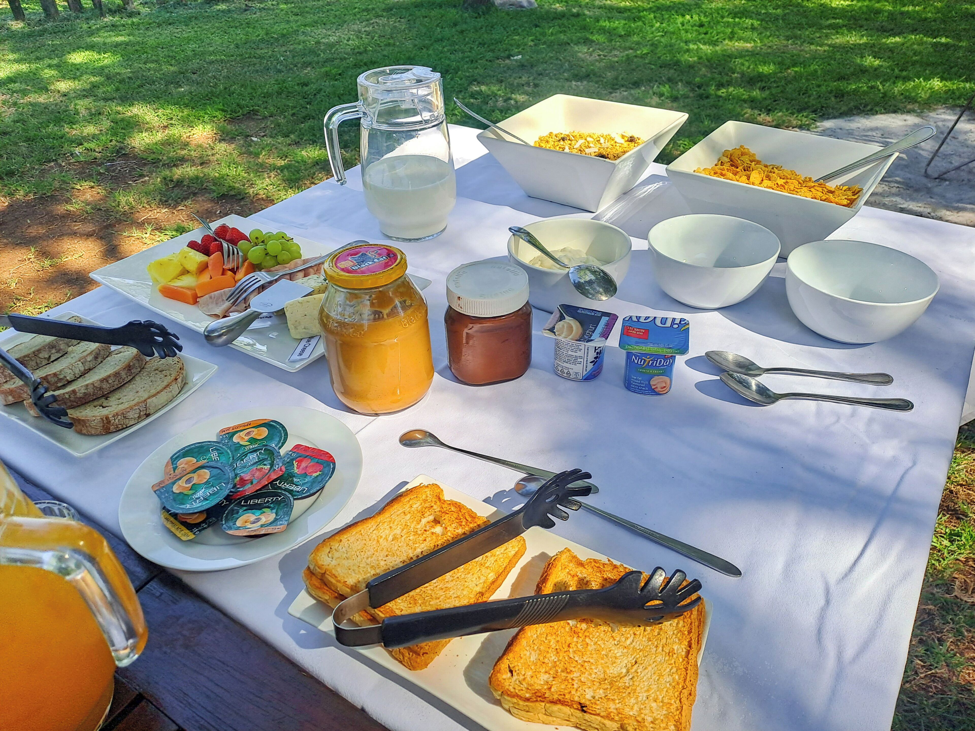 A picnic setup with food items, a pitcher, and utensils on a table.