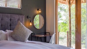 A bedroom with a bed, a bedside table, a mirror, and a window with blinds.