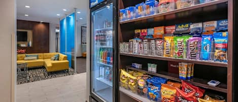 Un vestíbulo de hotel con zona de estar, un refrigerador lleno de aperitivos y estantes con distintos alimentos.