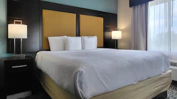 A hotel room with a large bed, two bedside tables with lamps, a headboard, and a window with curtains.