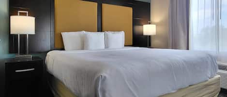 A hotel room with a large bed, two bedside tables with lamps, a headboard, and a window with curtains.