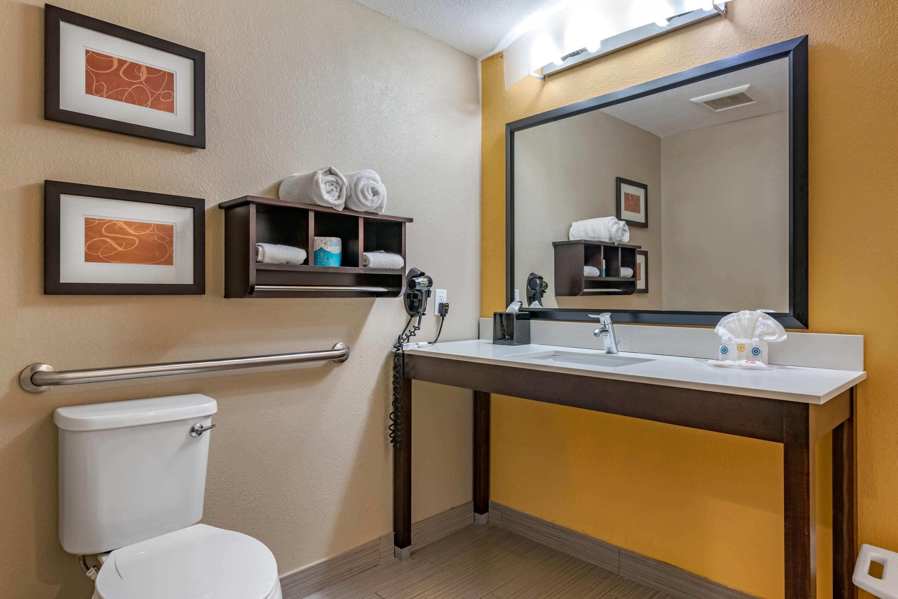 Un bagno d'albergo con un WC, un lavandino, uno specchio e spazio per asciugamani.