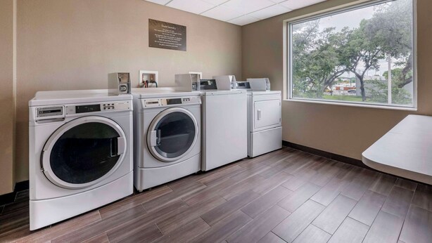 Une buanderie équipée de quatre machines à laver, d’un sèche-linge et d’une grande fenêtre donnant sur les arbres et les bâtiments environnants.