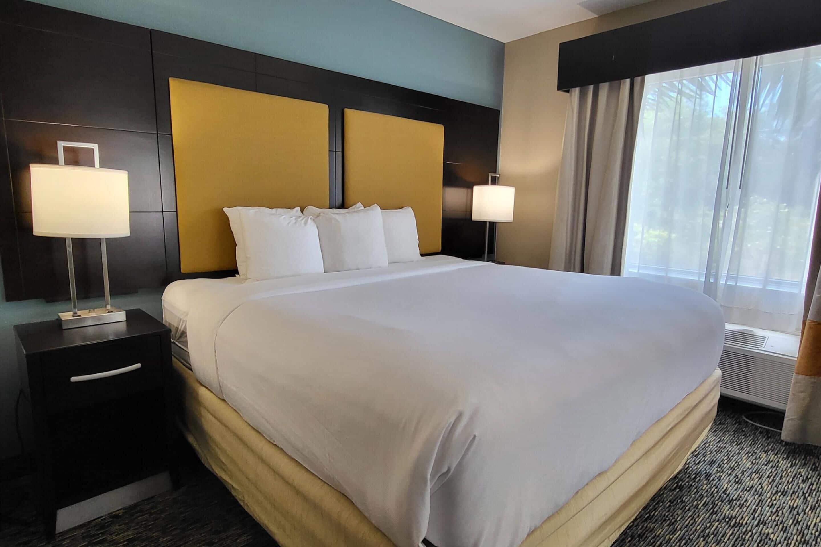 A hotel room with a large bed, two bedside lamps, a nightstand, and a window with curtains.