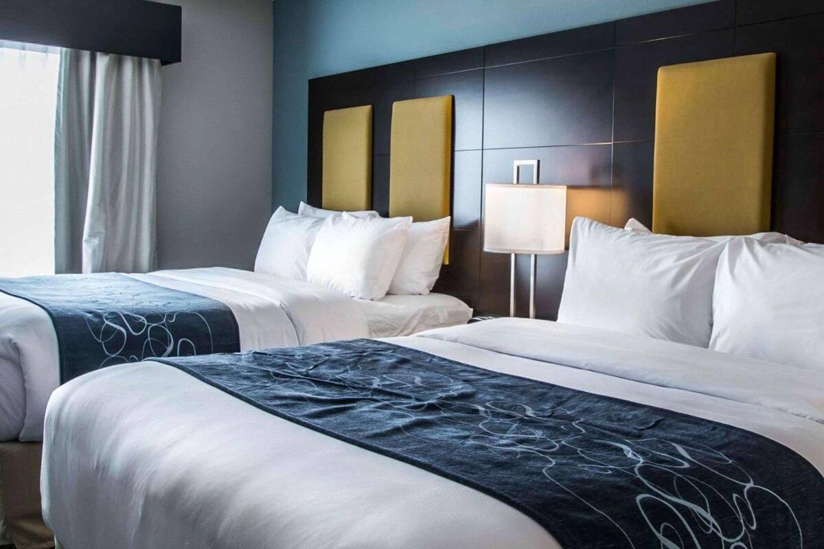 A hotel room with two beds, a dark headboard, a bedside lamp, and a window with curtains.