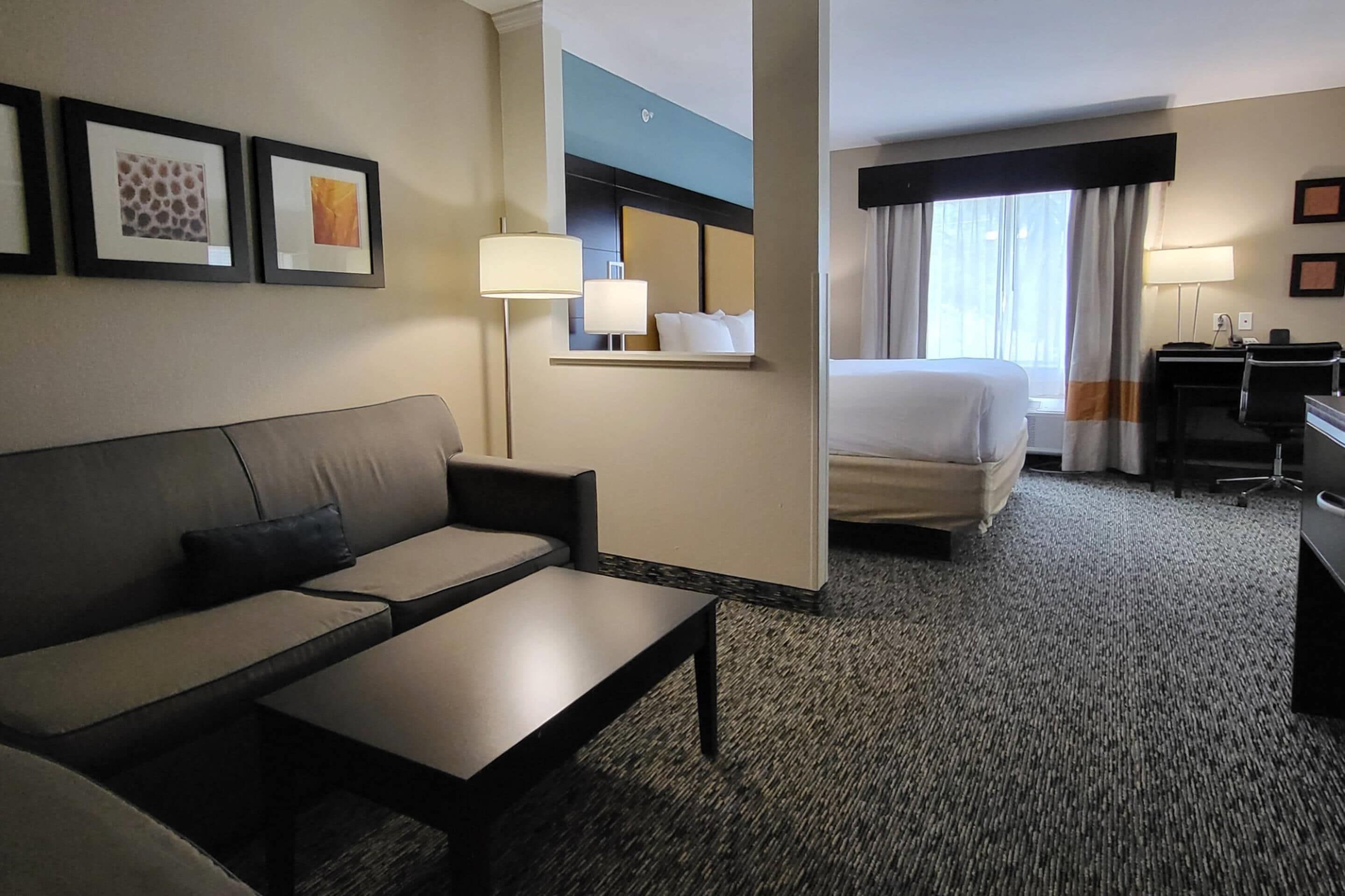 Ein Hotelzimmer mit Sofa, kleinem Tisch, Bett, Schreibtisch und einem Fenster mit Vorhängen.