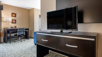 Une chambre d’hôtel avec un téléviseur à écran plat posé sur un bureau en bois foncé, une lampe de bureau, une chaise et un sol recouvert d’une moquette.