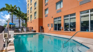 A swimming pool with a clear blue water, surrounded by a building with orange walls and large windows. - Comfort Suites Fort Lauderdale Airport South & Cruise Port (Dania Beach)