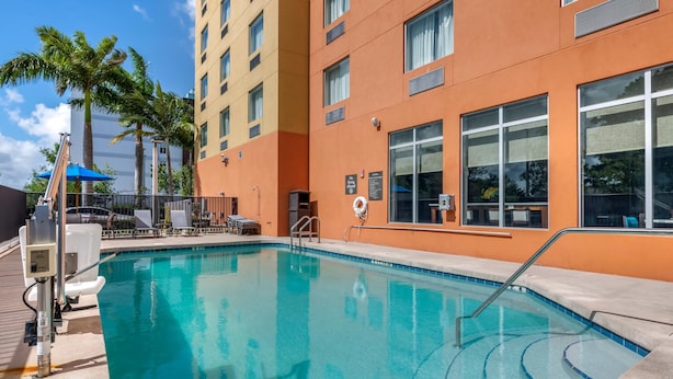 A swimming pool with a clear blue water, surrounded by a building with orange walls and large windows. - Comfort Suites Fort Lauderdale Airport South & Cruise Port (Dania Beach)