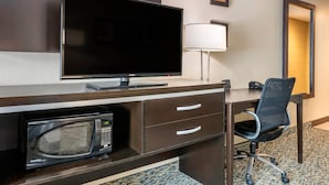 A hotel room with a flat-screen TV, a desk with a lamp, a microwave, and a chair.