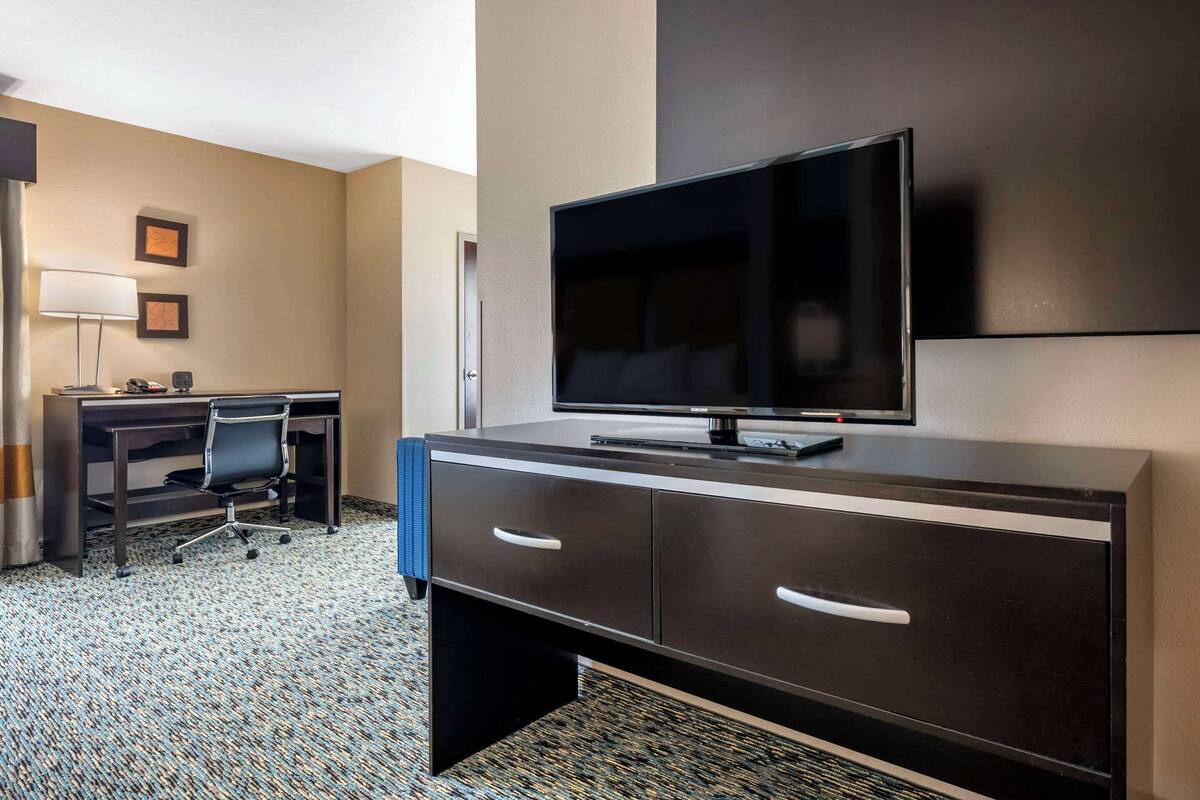 A hotel room with a dark wooden desk, a flat-screen TV, a lamp, and a chair.
