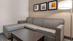 A hotel room with a gray sectional sofa, a small wooden coffee table, and three framed artworks on the wall. - Comfort Suites Fort Lauderdale Airport South & Cruise Port (Dania Beach)
